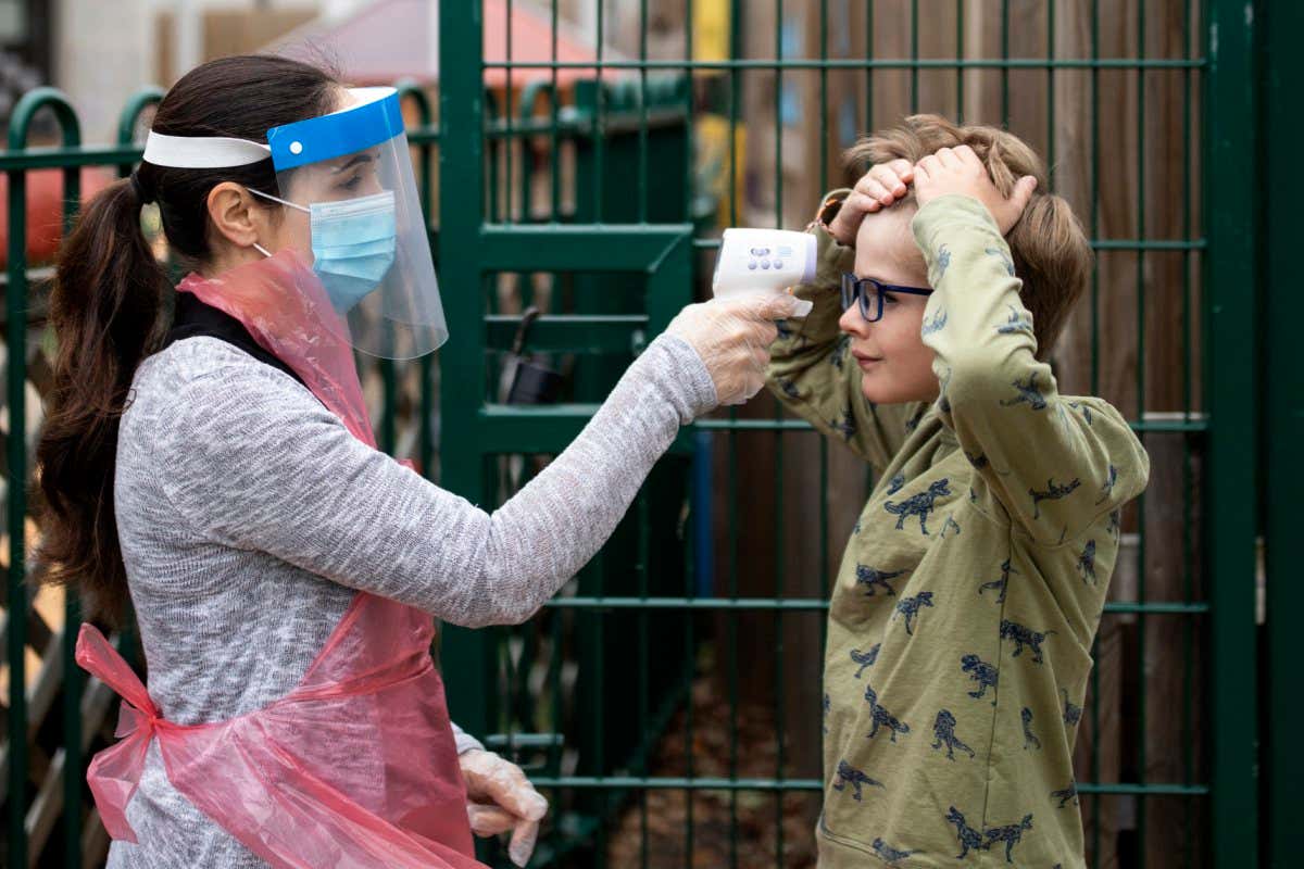 Staff wearing PPE take a child's temperature at a London school