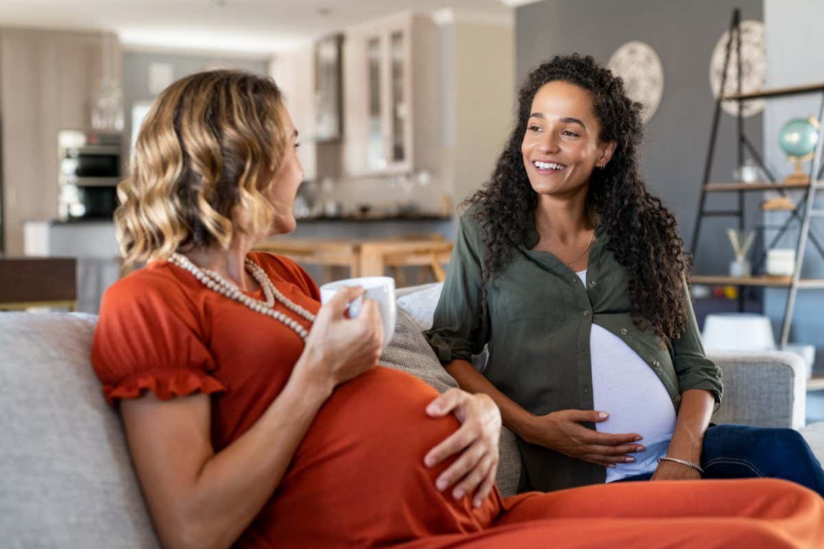 Two multiethnic pregnant women enjoying tea time at home. Smiling pregnant women talking and looking at each other. Happy girls both with a baby bump relaxing on couch and have a friendly conversation; Shutterstock ID 1773304790; purchase_order: -; job: -; client: -; other: -