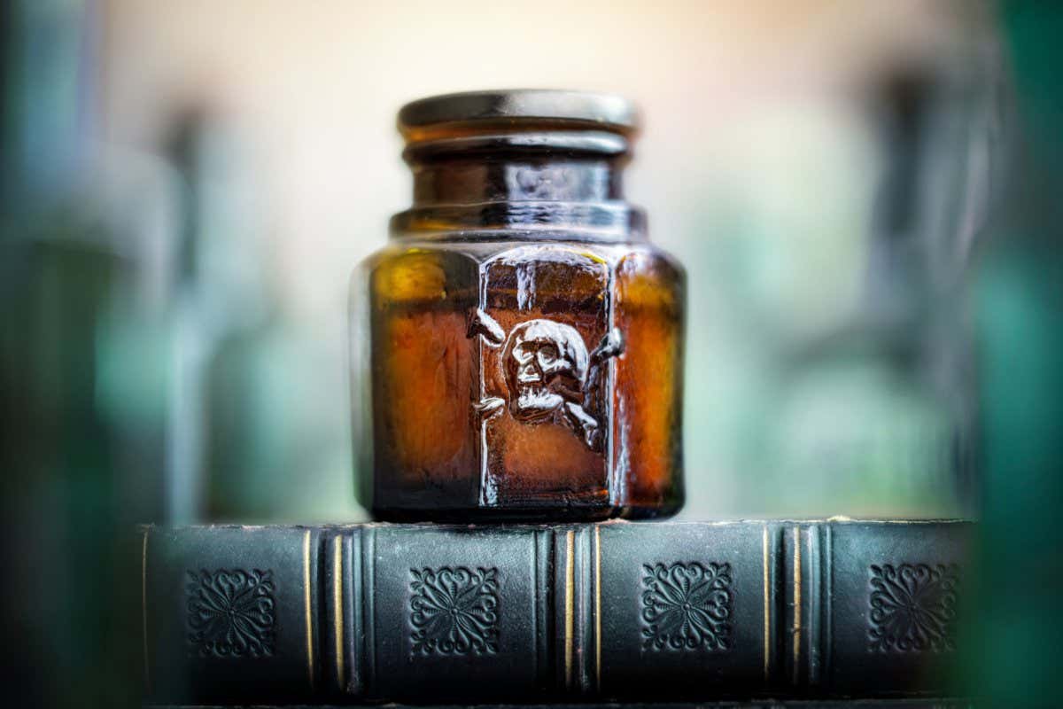 Glass poison bottle on book. Danger sign, symbol of death. Concept background on poison poisoning, pharmaceutical, chemistry, medical, old science topic.; Shutterstock ID 1950627238; purchase_order: -; job: -; client: -; other: -