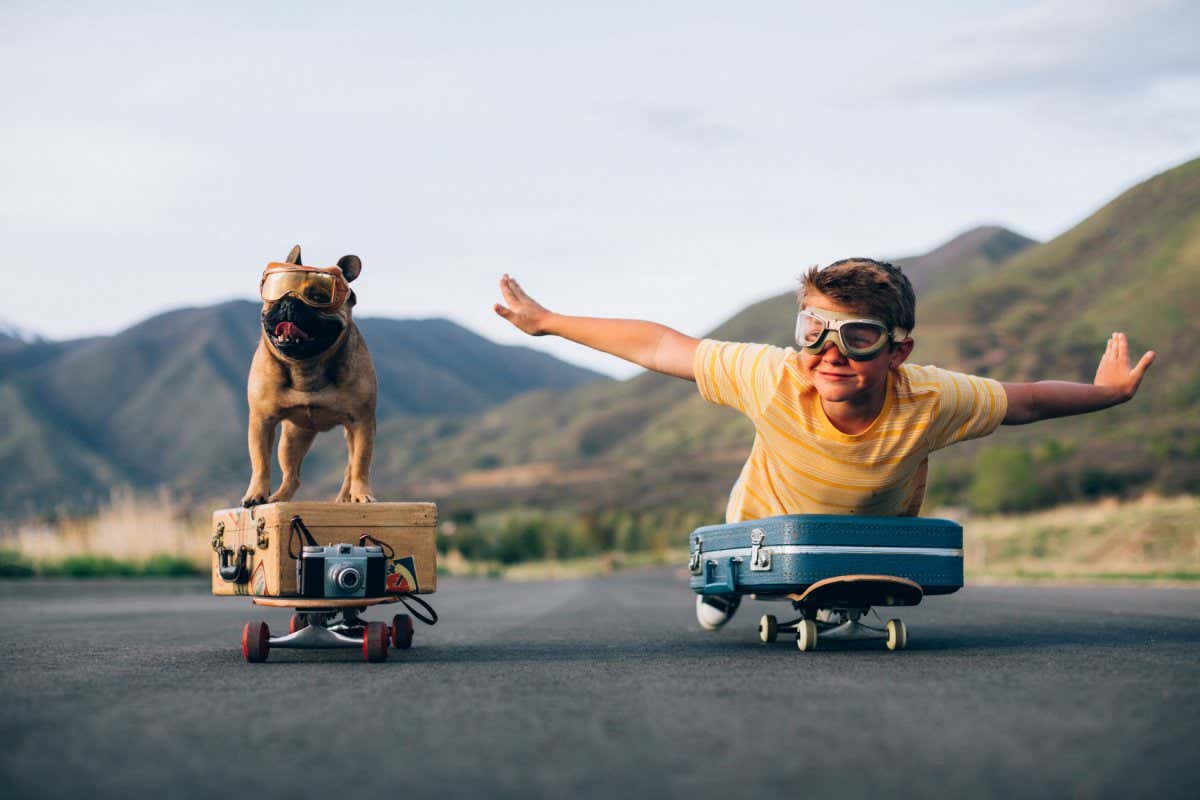 A young boy and his French Bulldog are ready to travel the world. They have put their suitcases on skateboards and are wearing flight goggles, ready to fly to new places and heights. Image taken in Utah, USA.