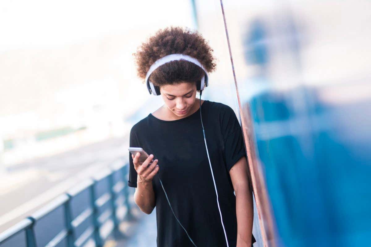 Young woman with headphones and smartphone leaning against wall