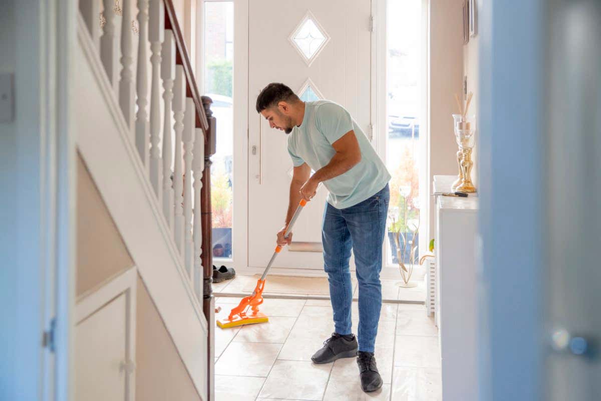 A front-view shot of a man cleaning the floor with a mop, he is wearing casual clothing.