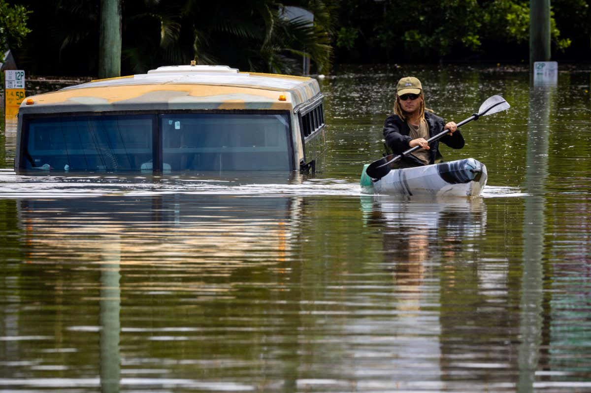 TOPSHOT - A man paddles his kayak next to a submerged bus on a flooded street in the town of Milton in suburban Brisbane on February 28, 2022. (Photo by Patrick HAMILTON / AFP) (Photo by PATRICK HAMILTON/AFP /AFP via Getty Images)
