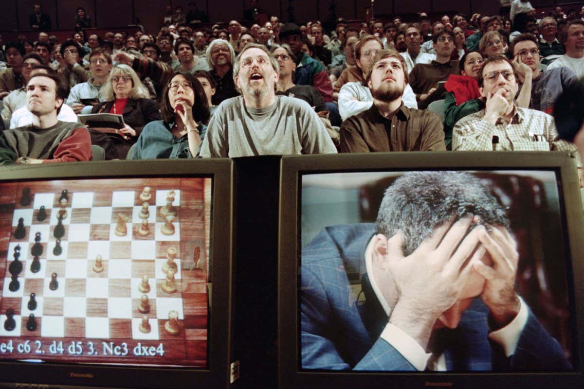 Chess enthusiasts watch World Chess champion Garry Kasparov on a television monitor as he holds his head in his hands at the start of the sixth and final match 11 May 1997 against IBM's Deep Blue computer in New York. Kasparov lost this match in just 19 moves giving overall victory to Deep Blue with a score of 2.5-3.5. / AFP / STAN HONDA (Photo credit should read STAN HONDA/AFP via Getty Images)