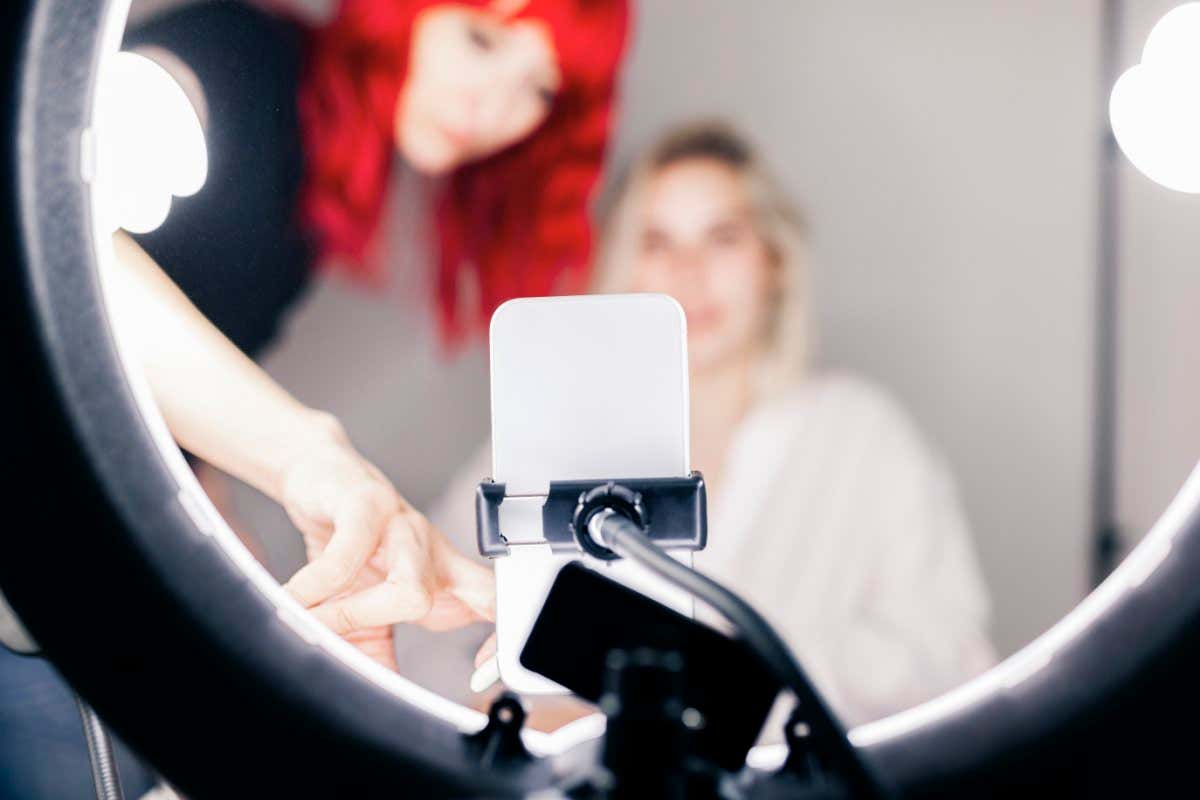 Young female bloggers shooting a beauty and makeup video at home with their cell phones and light rings.