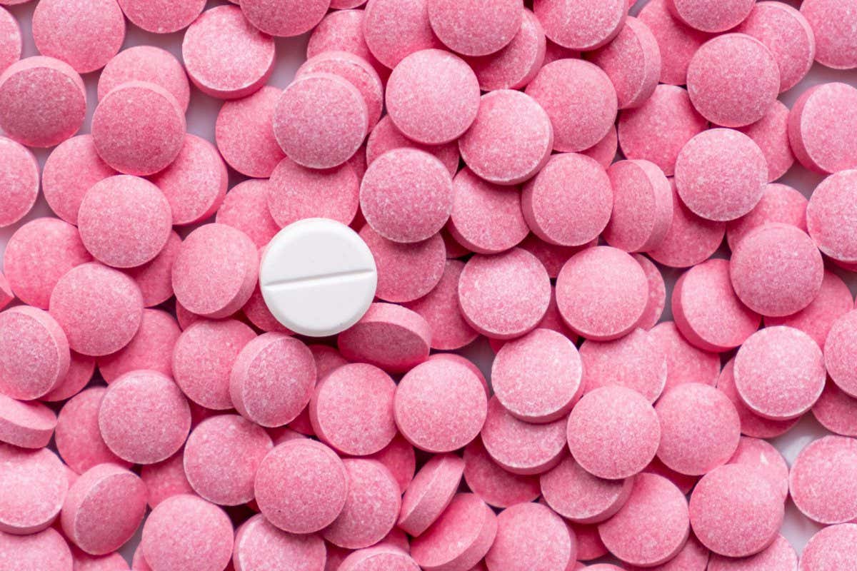 2AD2YRB Pile of pink pills and around a white one. Medication, self-treatment or placebo concept: one tablet is different from the lot of others