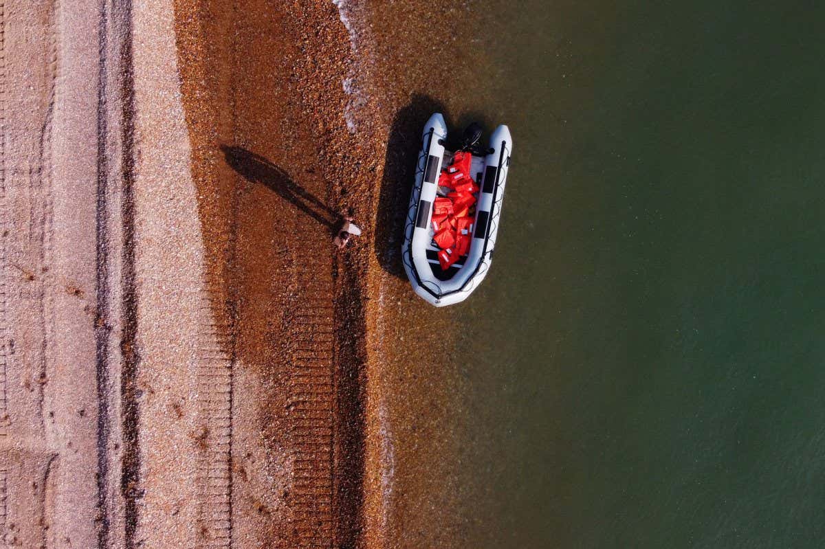 TOPSHOT - An aerial picture shows a man using a mobile telephone whilst standing next to a recently abandoned inflatable boat, used by migrants to cross the Straits of Dover from France to Deal on the south east coast of England, on September 14, 2020, after the migrants arrived on the beach. - Nearly 1,500 migrants and asylum-seekers arrived in Britain by small boats in August, according to an analysis by the domestic Press Association news agency. (Photo by BEN STANSALL / AFP) (Photo by BEN STANSALL/AFP via Getty Images)