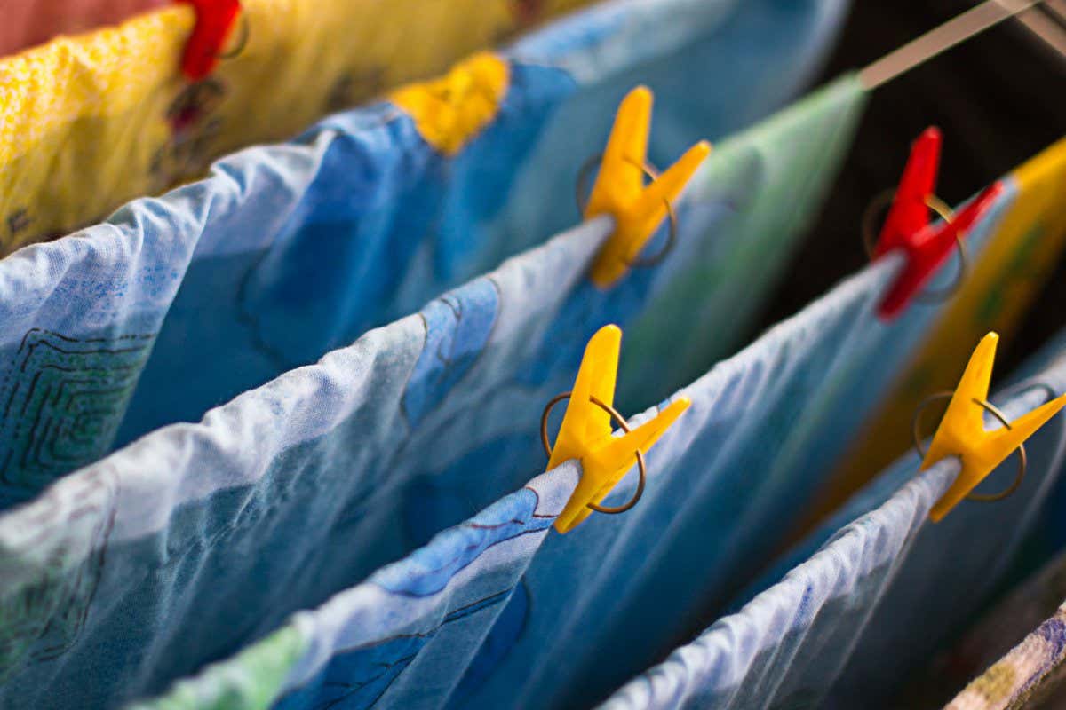 Colorful clean bed linen and towels after washing are hung on the bars of the dryer and secured with clothespins. General cleaning, Laundry drying, compact dryer for the house. Selective focus; Shutterstock ID 1795609045; purchase_order: -; job: -; client: -; other: -