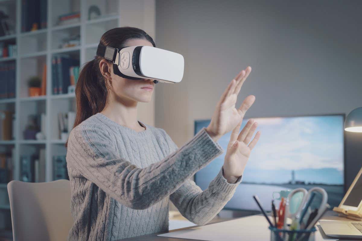 Young woman sitting at desk and wearing a VR headset, she is interacting with virtual reality; Shutterstock ID 2121732383; purchase_order: -; job: -; client: -; other: -