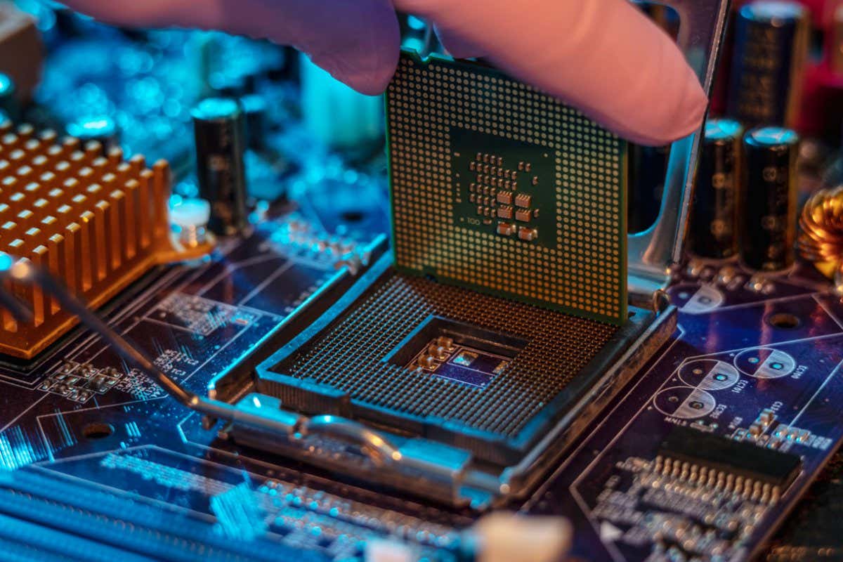 2F5G0XB The engineer's gloved hand is holding the CPU chip against the background of the motherboard. Concept of high-tech hardware microelectronics