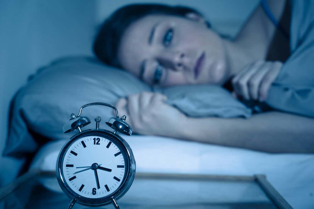 Sleepless and desperate beautiful caucasian woman awake at night not able to sleep, feeling frustrated and worried looking at clock suffering from insomnia in sleep disorder concept.; Shutterstock ID 1337363627; purchase_order: -; job: -; client: -; other: -