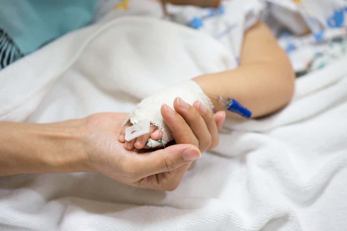 A stock image of a person holding a child's hand in hospital