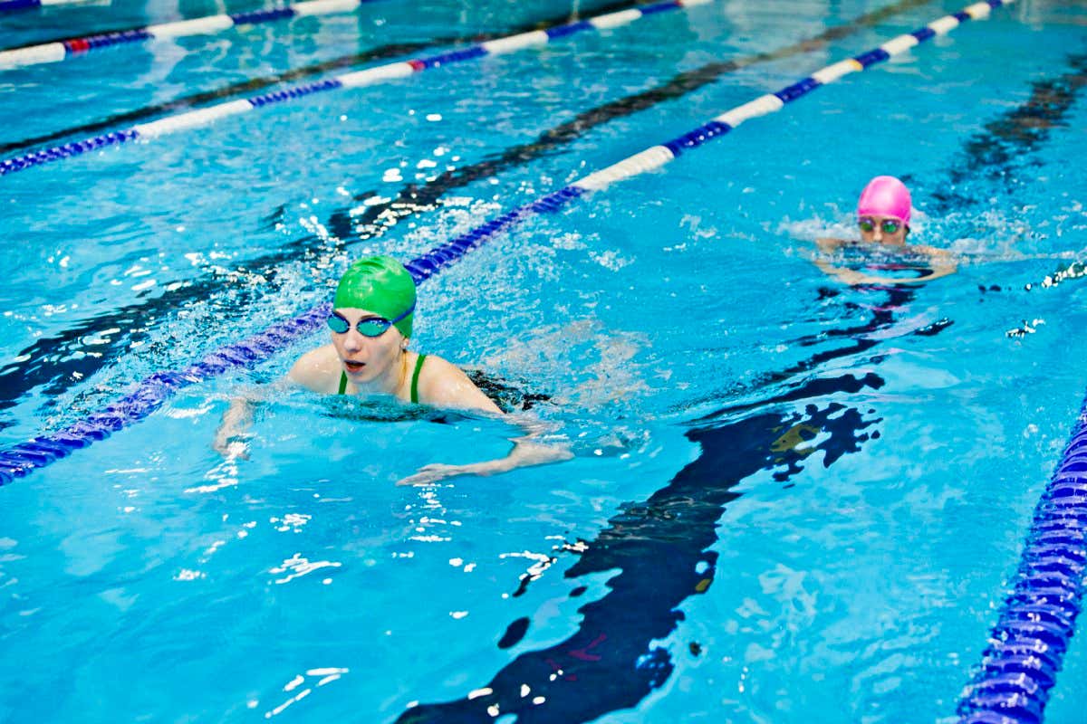 Young women swim breaststroke, wearing swimming caps and goggles.