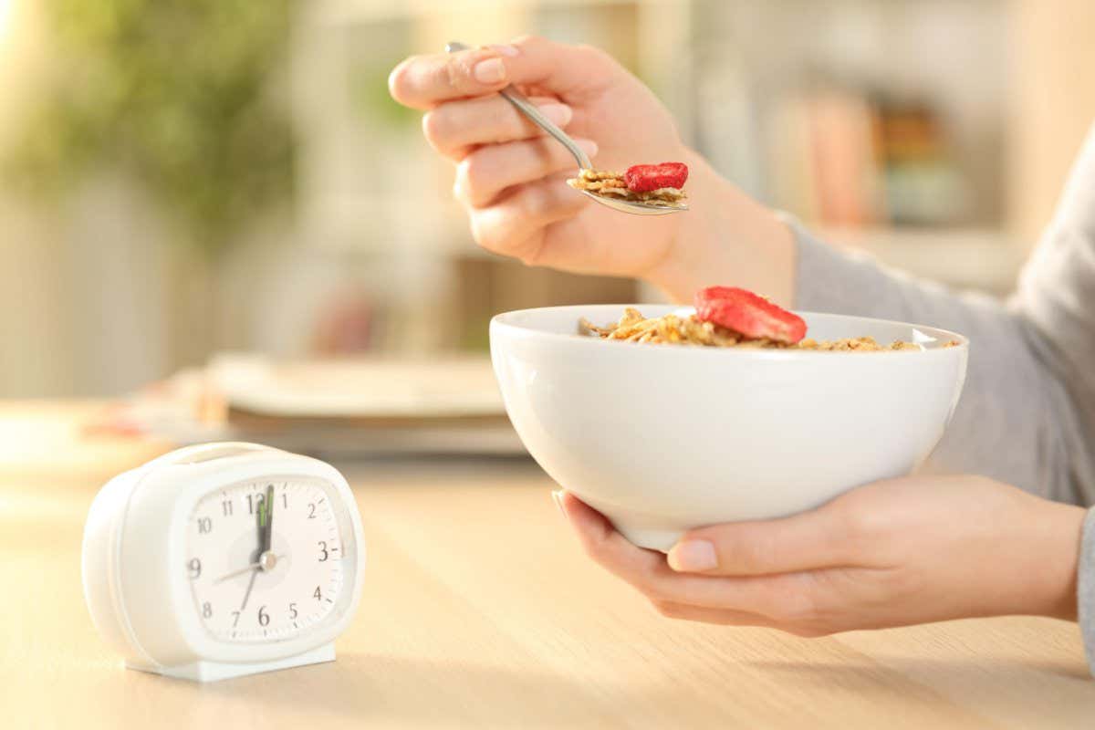 2BKMNTM Close up of woman hands eating cereal bowl with fruit after intermittent fasting sitting on a table at home