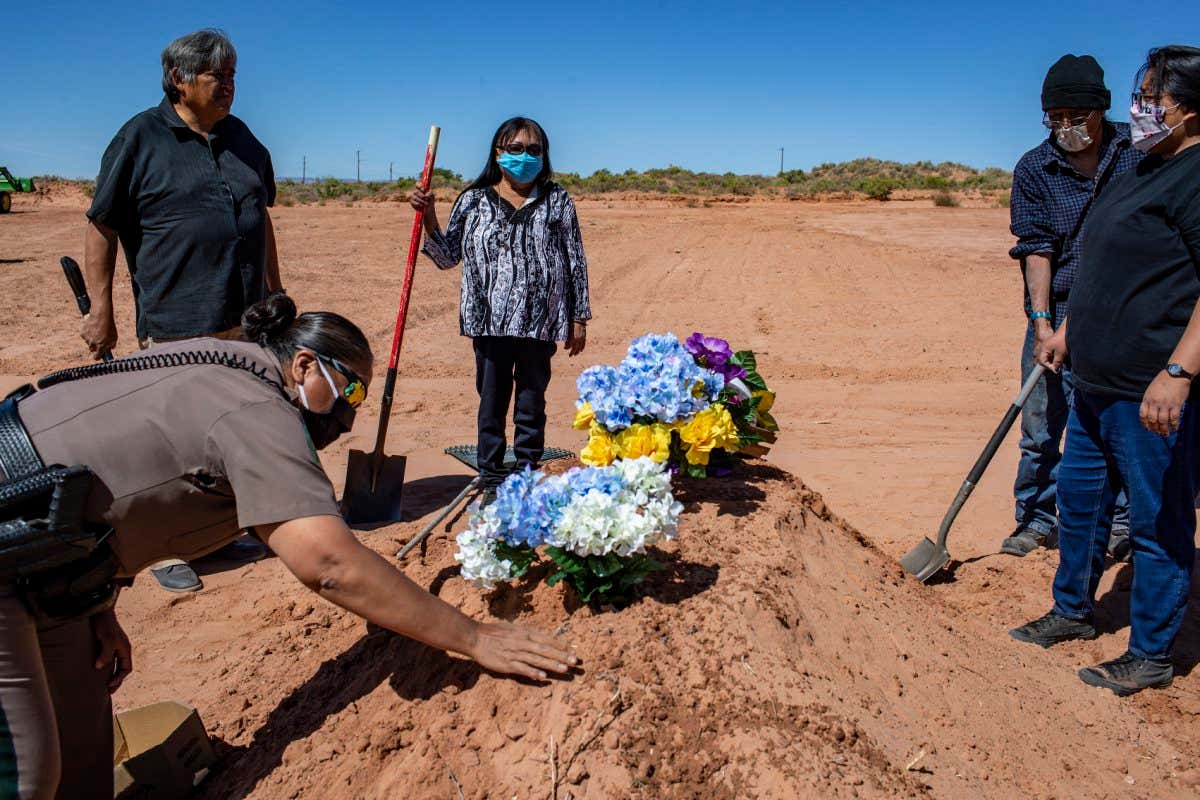 A Navajo Nation police officer smooths dirt over the grave of a person who died of covid-19 in Tuba City, Arizona