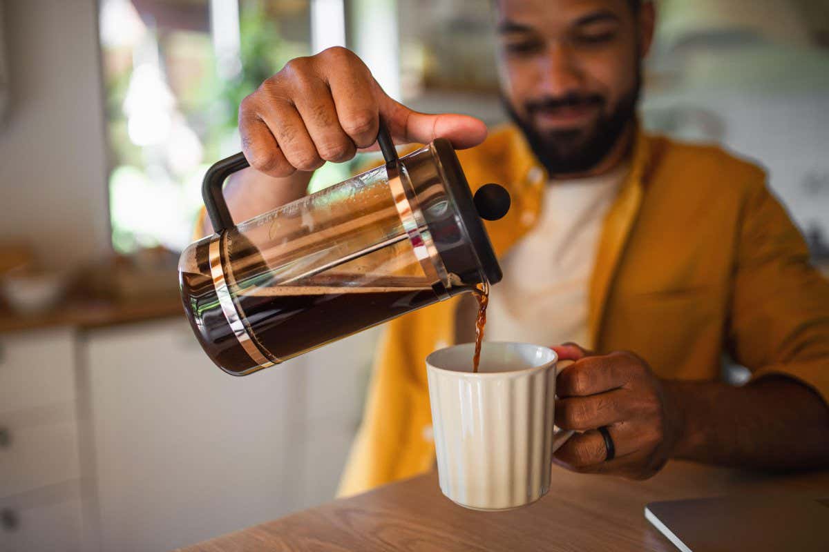 2GE29AM Young man pouring coffee from french press working indoors, home office concept.