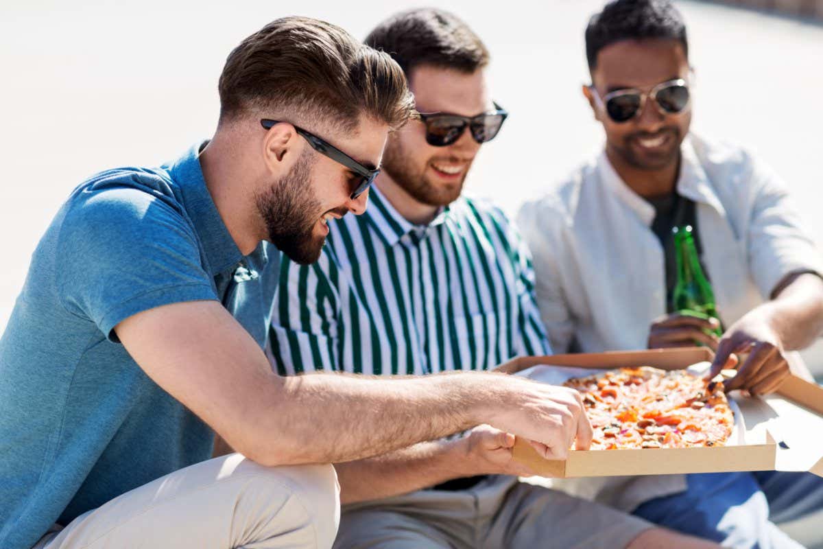 Male friends eating pizza with beer on street