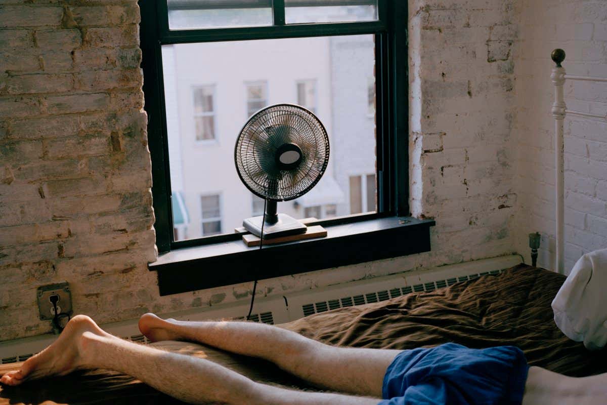Man lying on bed in front of fan