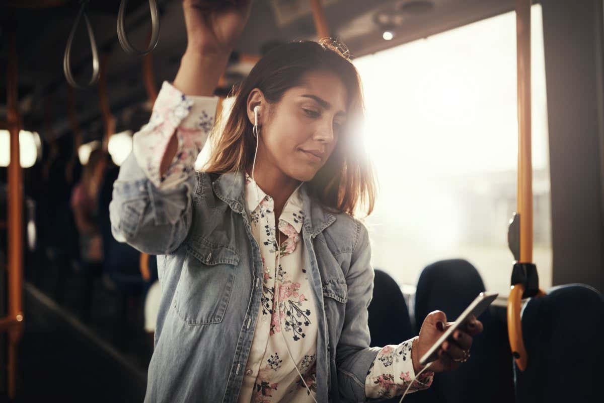 Young woman smiling while riding on a bus listening to music on a smartphone