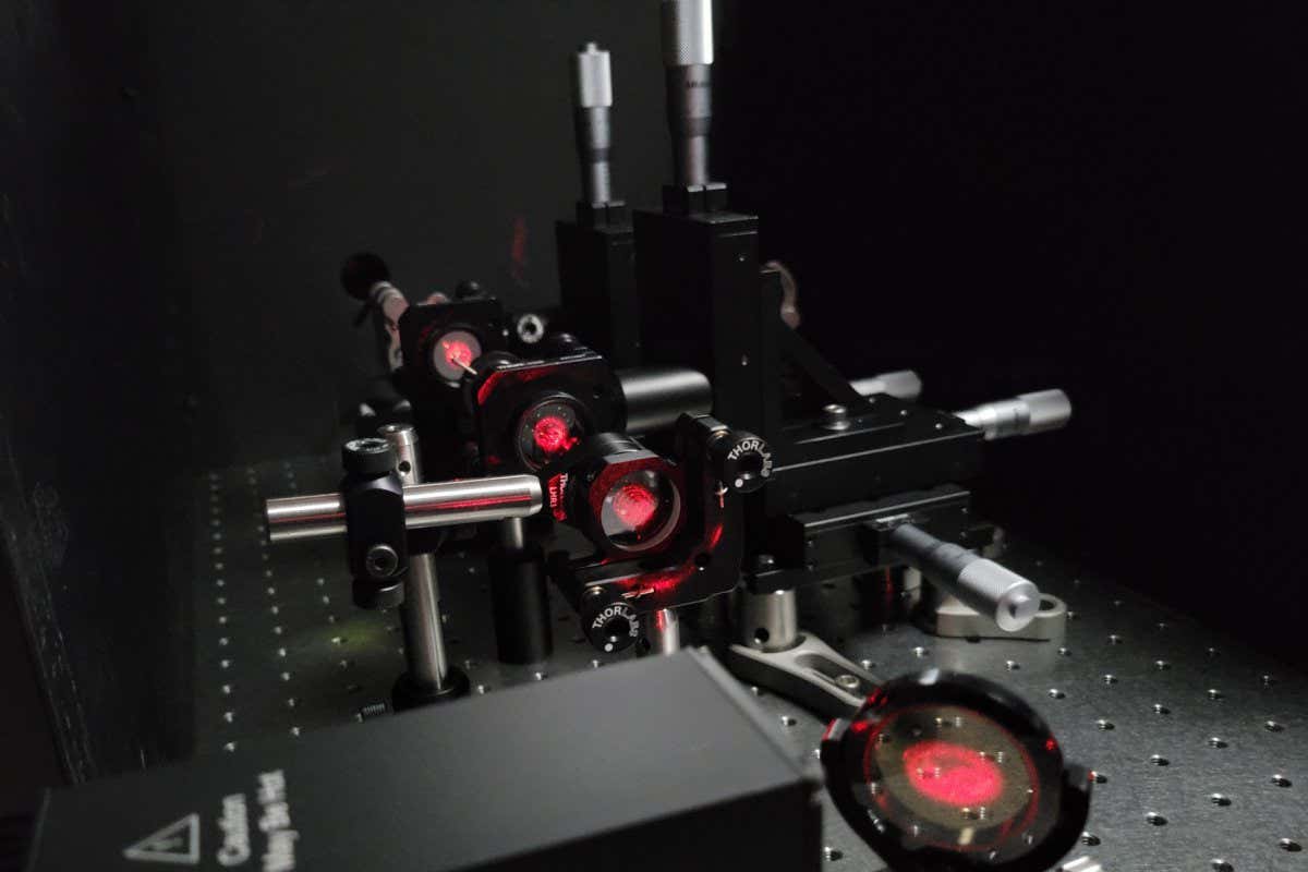 A beam of red light shines through a series of four lenses within a telescope-like device