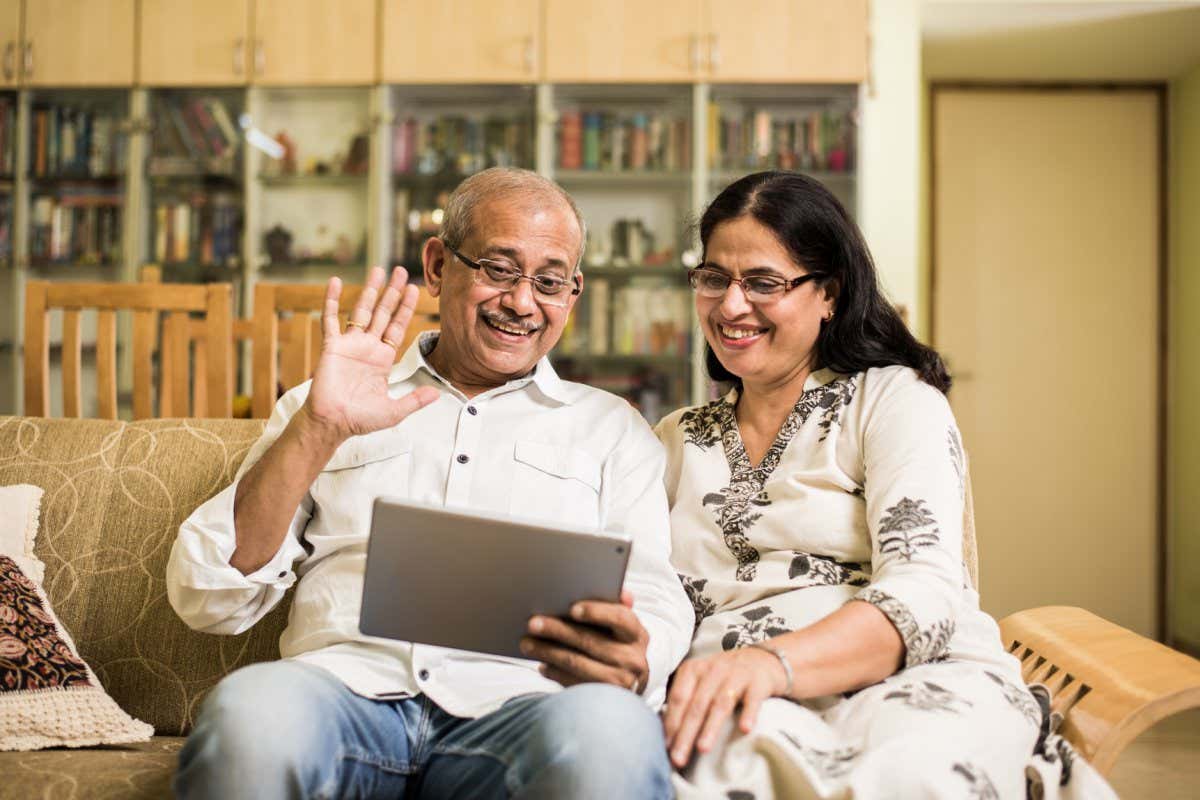 Indian/asian Senior couple video chatting on tablet/computer while sitting at couch or in garden at home, selective focus