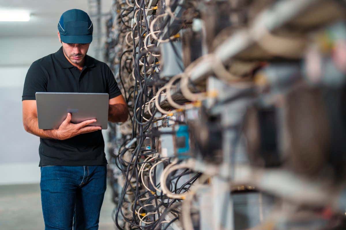 Man holding laptop next to bank of computer equipment