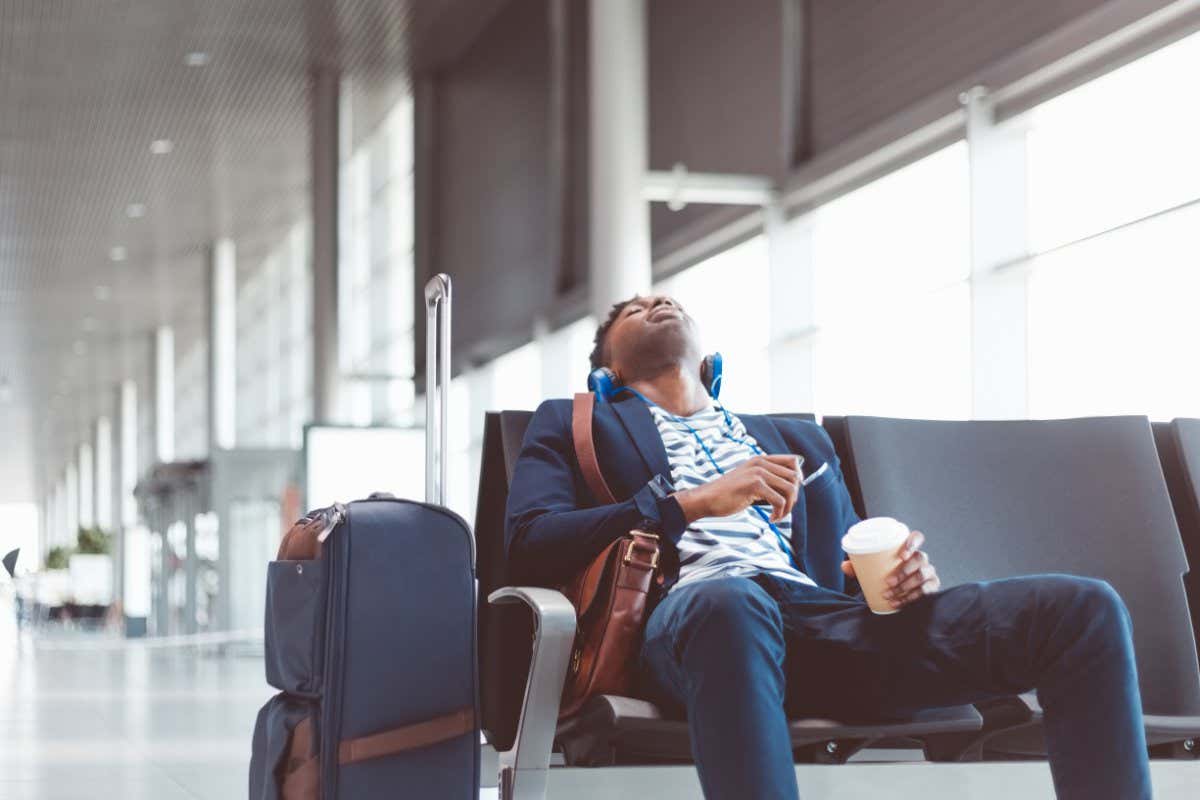 Young african man sitting at airport lounge and sleeping, waiting for flight at airport departure area.