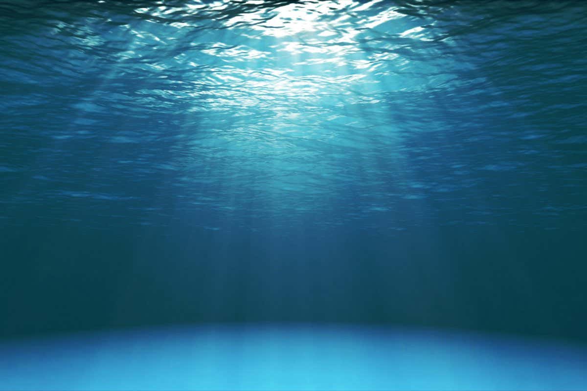 Dark blue ocean surface seen from underwater. Waves underwater and rays of sunlight shining through