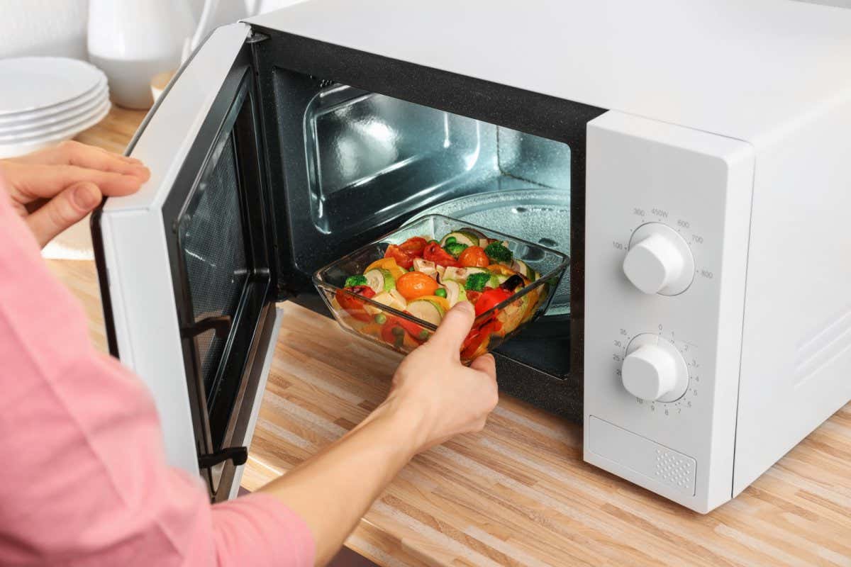 Woman putting bowl with vegetables in microwave oven, closeup; Shutterstock ID 1011440542; purchase_order: -; job: -; client: -; other: -