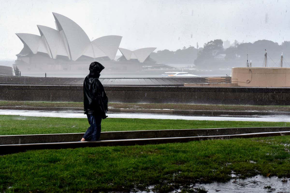 A woman walks before the Opera House while it rains in Sydney on October 6, 2022. (Photo by Muhammad FAROOQ / AFP) (Photo by MUHAMMAD FAROOQ/AFP via Getty Images)