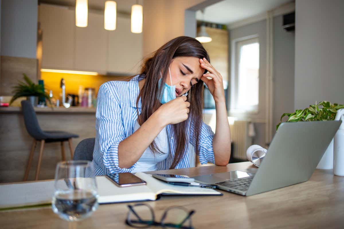 Woman working in the office and having difficulties breathing with face mask, she is pulling the mask down. The woman had to remove the mask to breathe after having to wear it for a long time