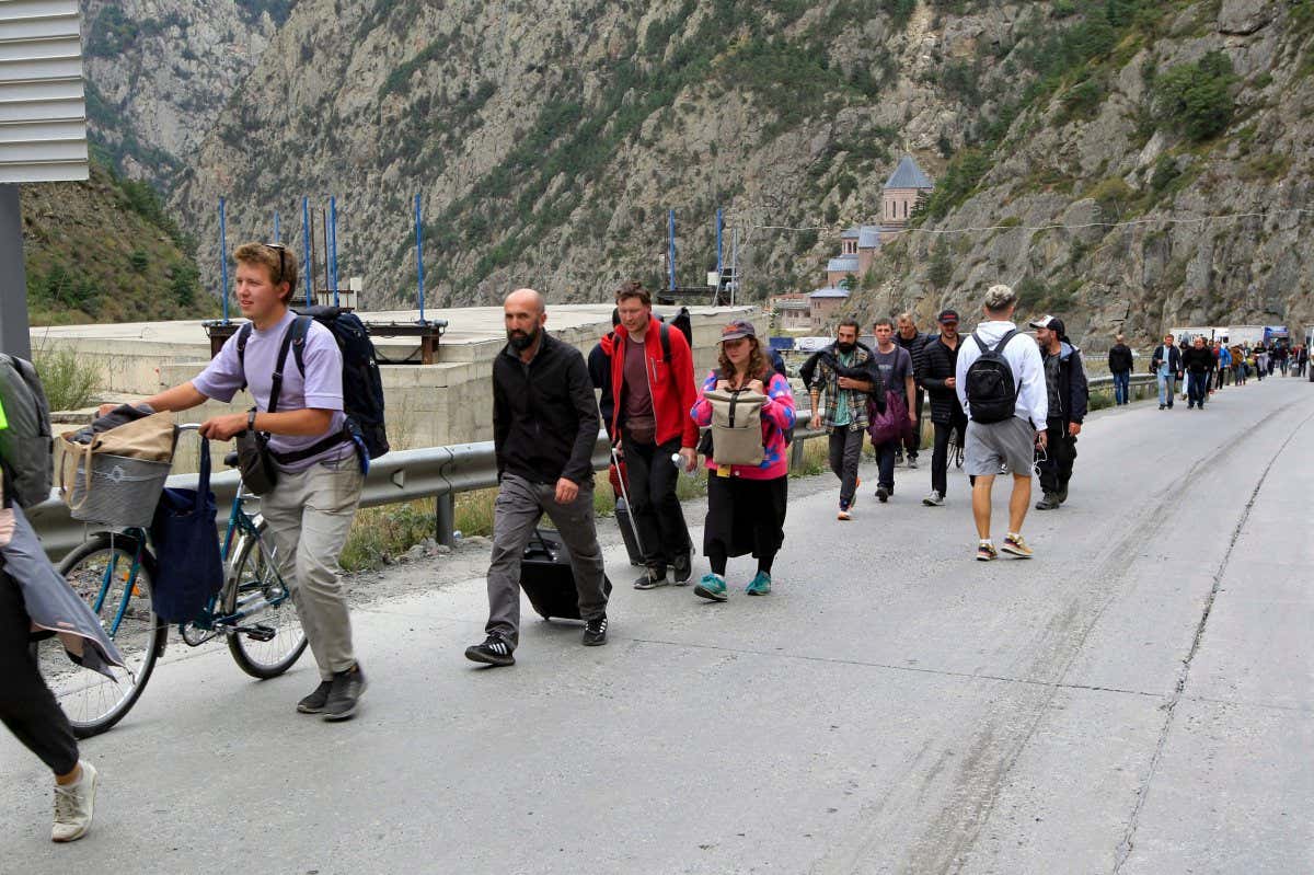 A long line of people walk in the same direction along a roadside in a mountainous region of the border between southwestern Russia and Georgia.