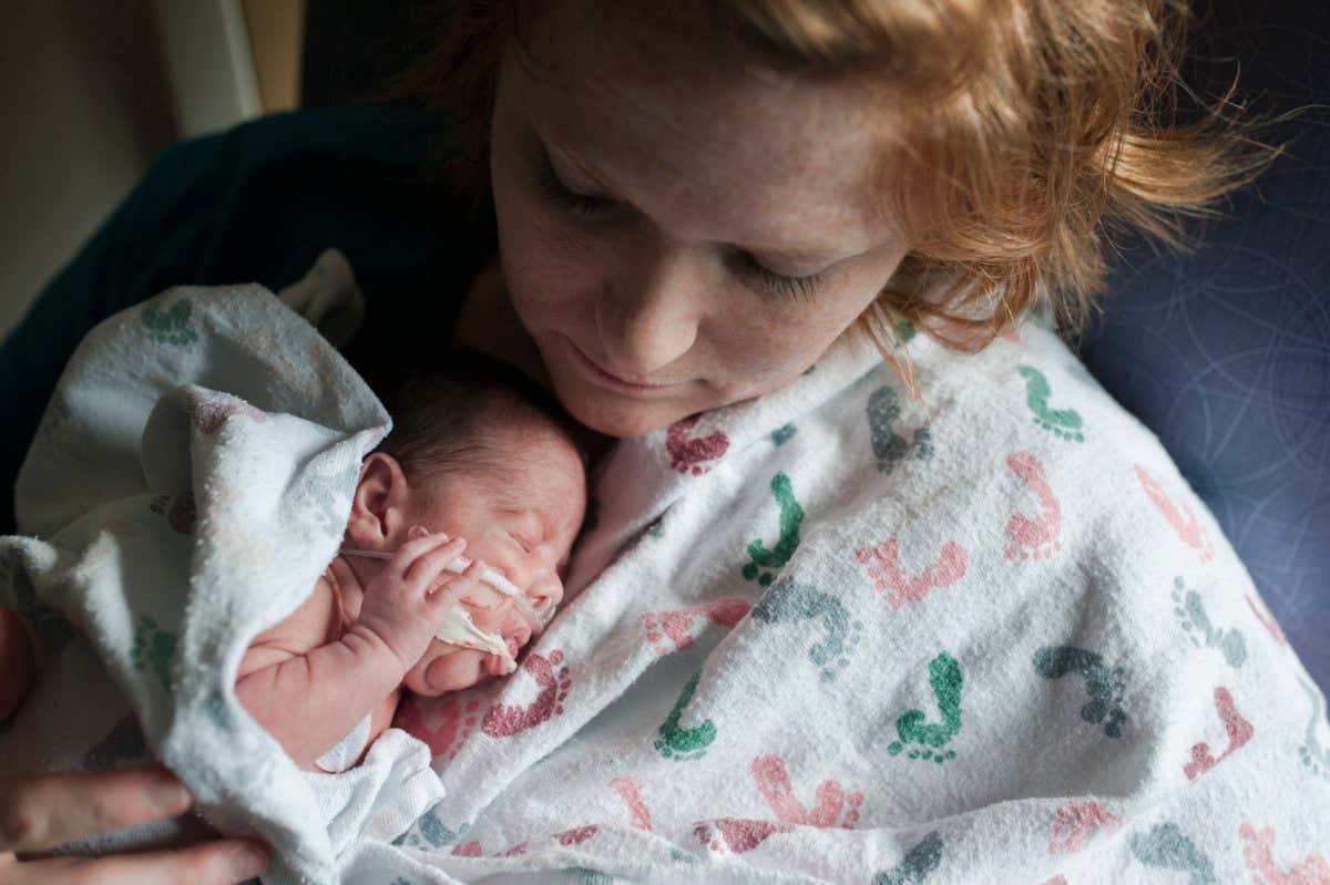 A baby in a neonatal intensive care unit is held by its mother