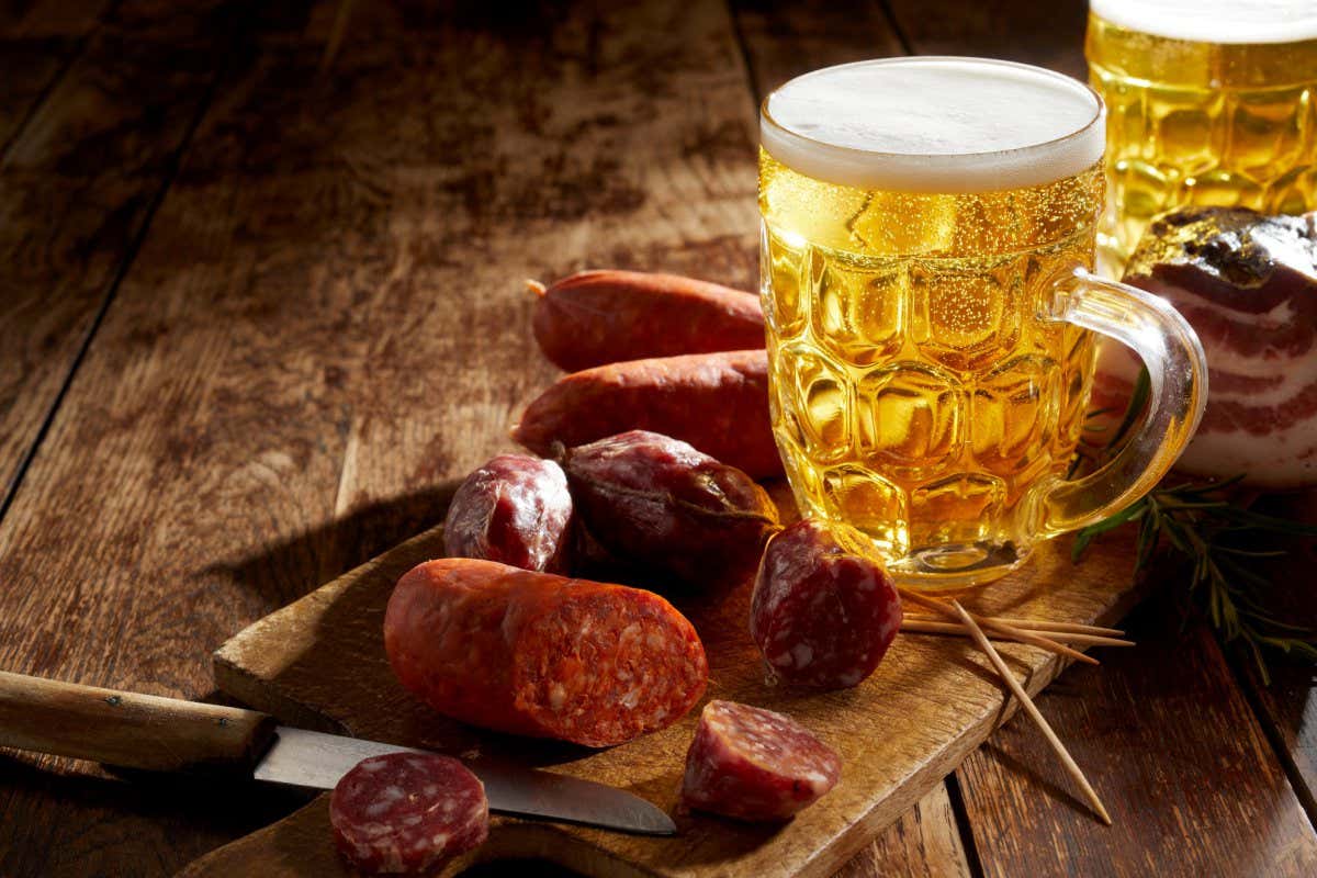 Tankard of refreshing cold beer with spicy sausage on a cutting board on a rustic table in a bar or pub with shadowy light and copyspace; Shutterstock ID 2052738722; purchase_order: -; job: -; client: -; other: -