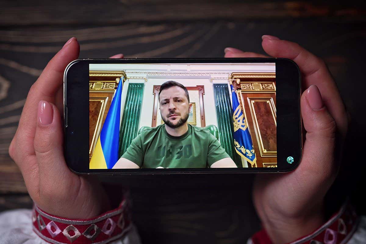 August 2022 - Kyiv, Ukraine. Watching online speech of President Volodymyr Zelenskiy on smartphone on wooden table background. News from front