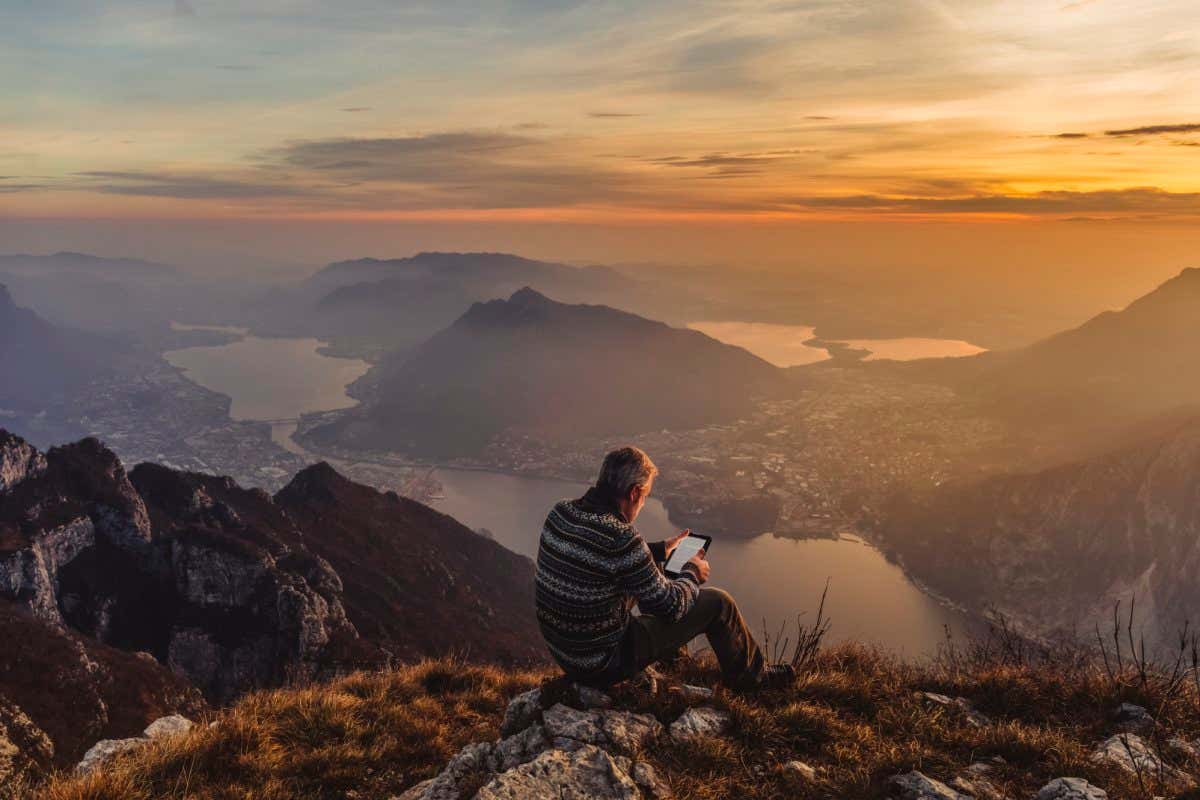 Man hiker solo on the mountain during golden hour reading e-book