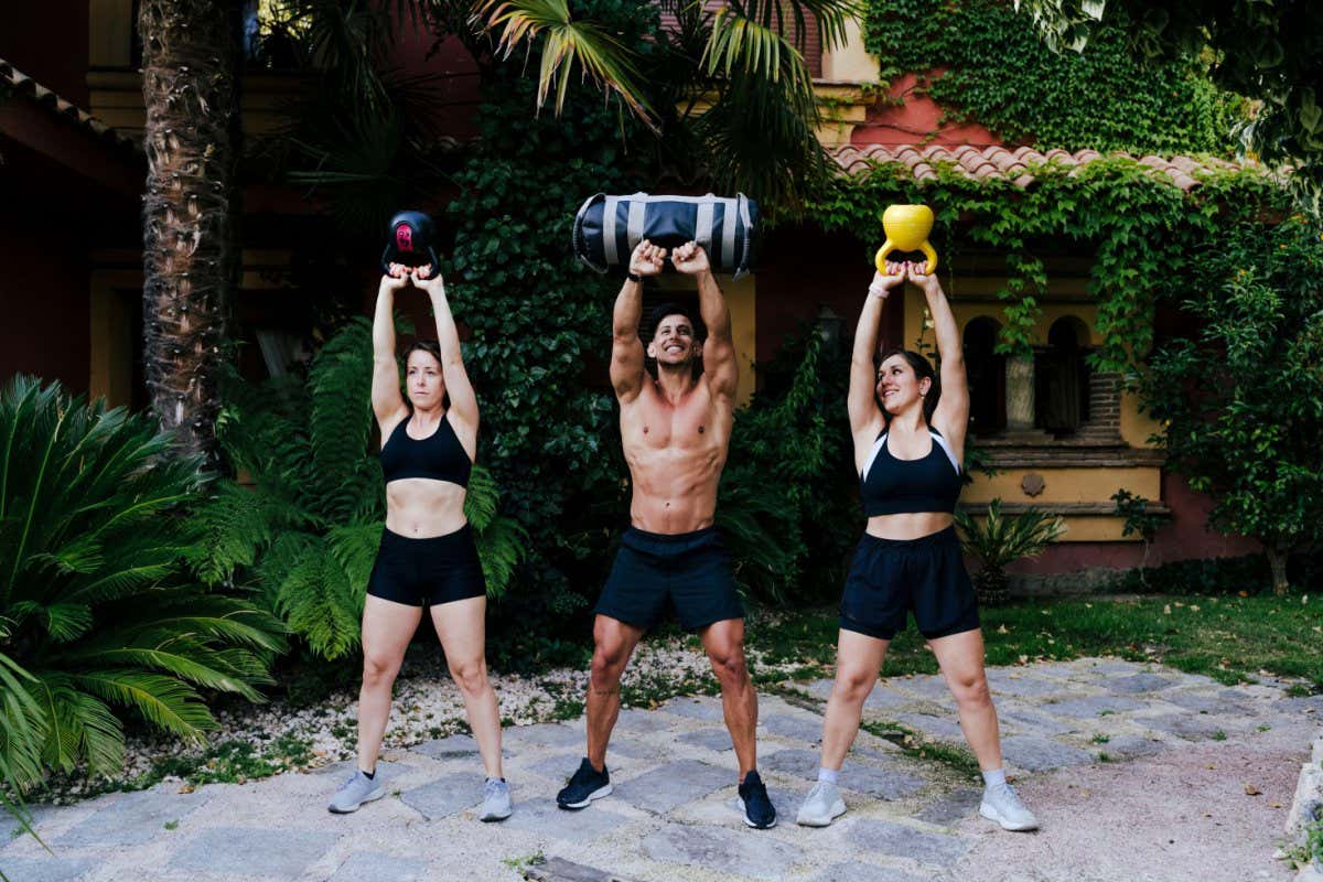 2CTJXXG Male fitness instructor with women lifting weights while standing in yard