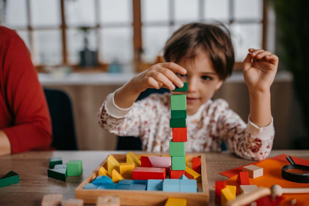 Two people, little girl playing with toy blocks, her mother is sitting next to her at home.