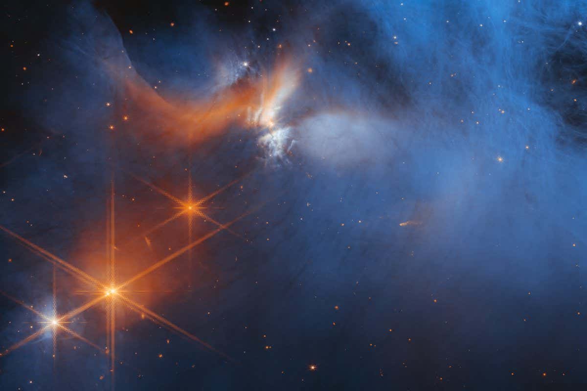 This image by NASA?s James Webb Space Telescope?s Near-Infrared Camera (NIRCam) features the central region of the Chamaeleon I dark molecular cloud, which resides 630 light years away. The cold, wispy cloud material (blue, center) is illuminated in the infrared by the glow of the young, outflowing protostar Ced 110 IRS 4 (orange, upper left). The light from numerous background stars, seen as orange dots behind the cloud, can be used to detect ices in the cloud, which absorb the starlight passing through them.