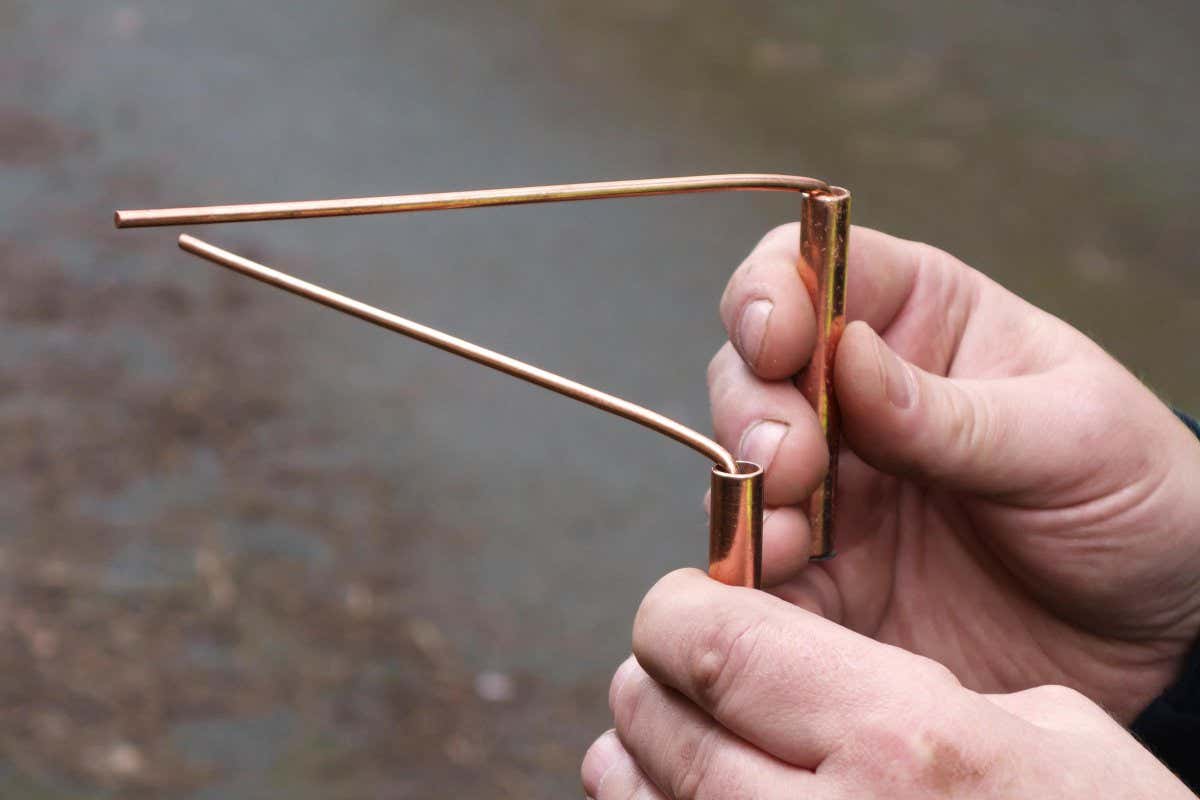 A water engineer uses copper divining rods to trace the course of an underground pipe