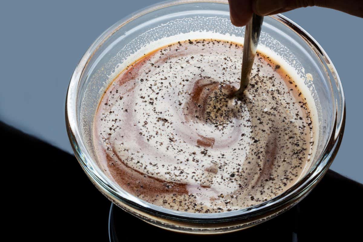 EX0YM9 Stirring tomato sauce and black pepper in a glass bowl with spoon
