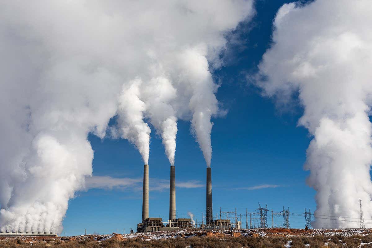 Three smokestacks from a coal-burning power plant send up plumes of white smoke into a blue sky