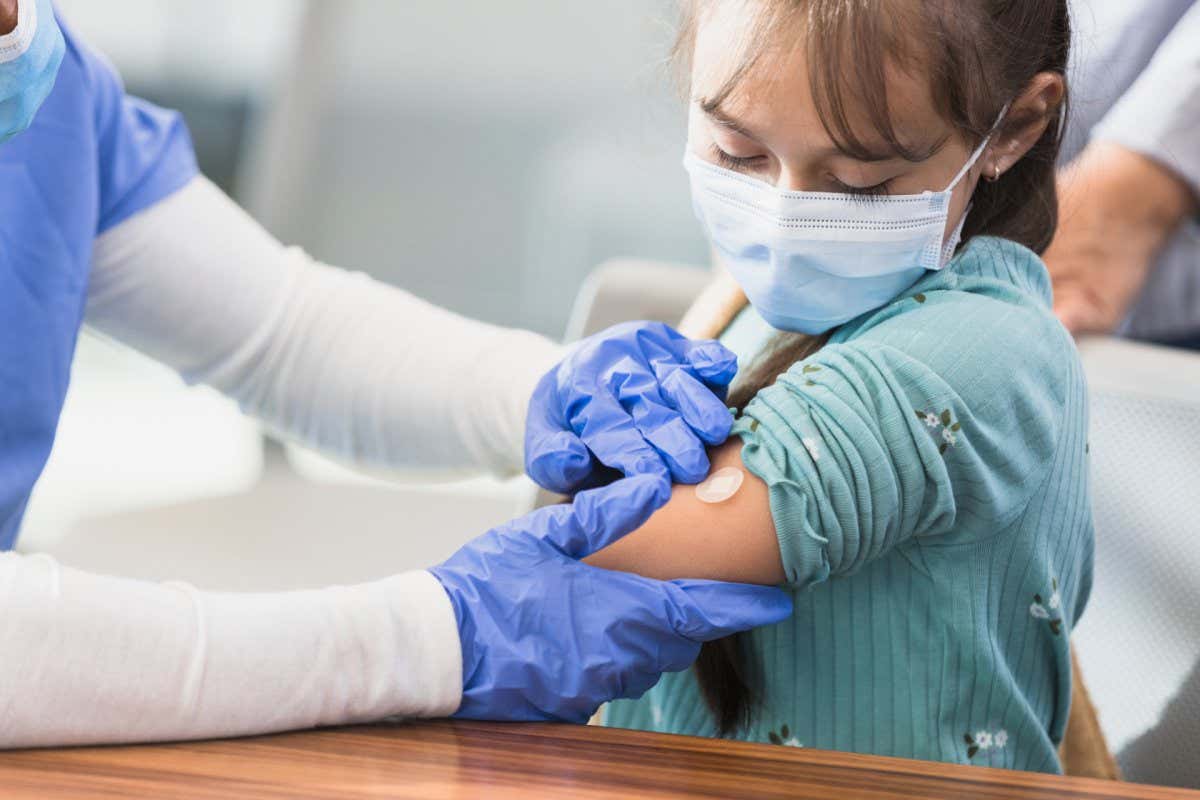 The young patient watches the nurse put a bandage on her injection site.