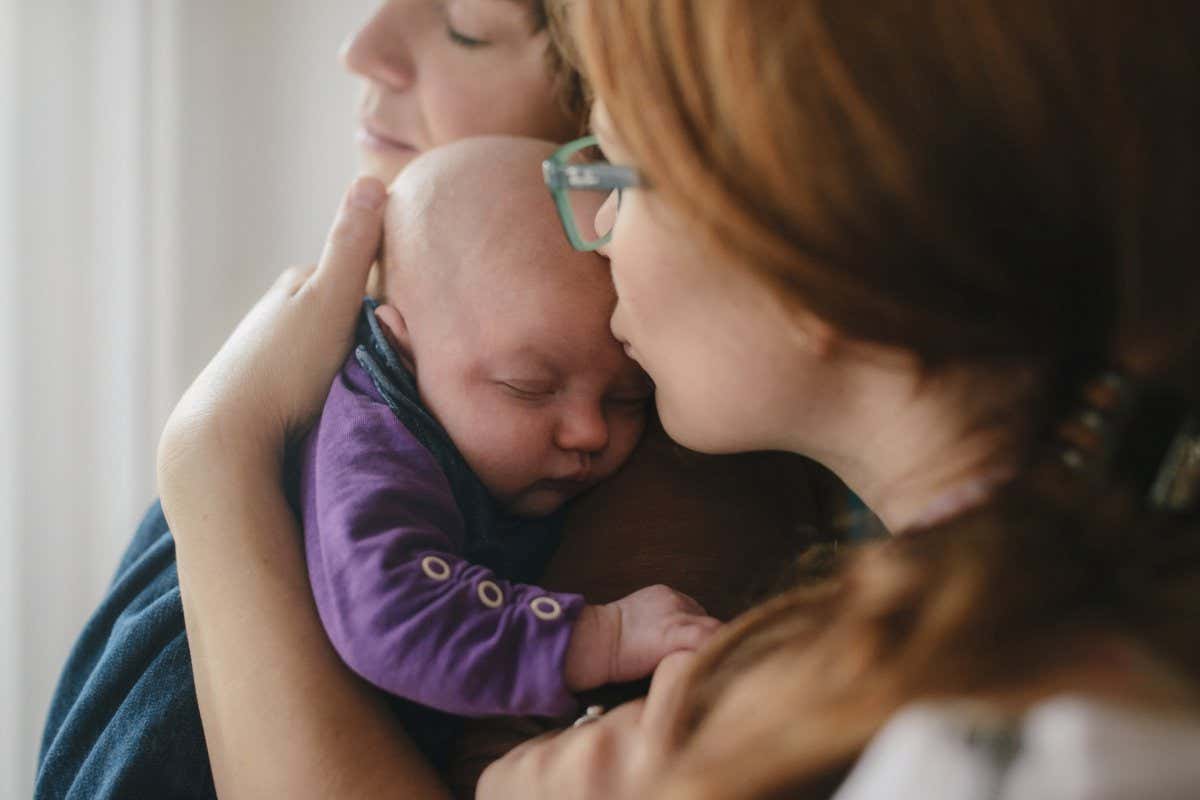 Lesbian couple with newborn child hugging.