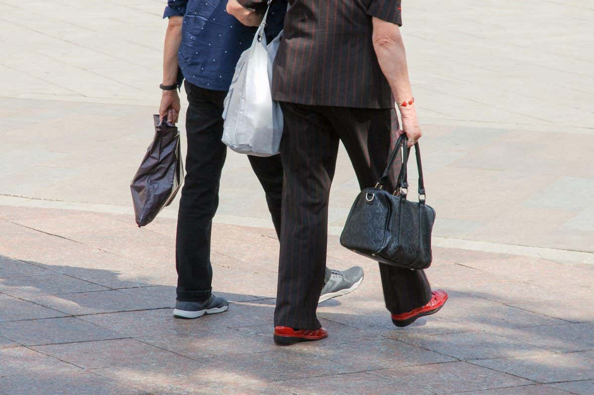 Two elderly women walking across pedestrian are, back view