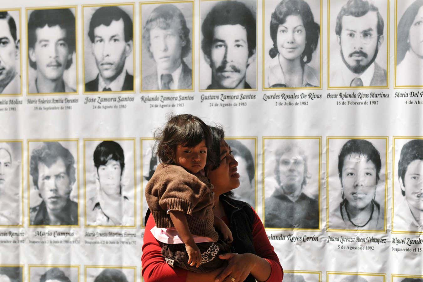 A woman with her daughter observes the pictures of people who lost their lives during the Guatemalan civil war, as forensic anthropologists from the Forensic Anthropology Foundation of Guatemala (FAFG) exhume the bodies of one of four mass graves in La Verbena cemetery, in Guatemla City on March 6, 2010, as part of a search to find the 889 people who disappeared during the internal armed conflict (1960-1996). AFP PHOTO/Johan ORDONEZ (Photo credit should read JOHAN ORDONEZ/AFP via Getty Images)