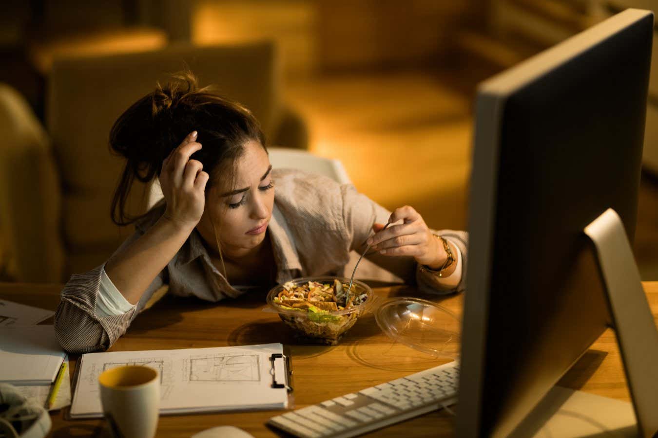 Distraught woman having salad for dinner while working on computer in the evening at home. ; Shutterstock ID 1581071689; purchase_order: -; job: -; client: -; other: -