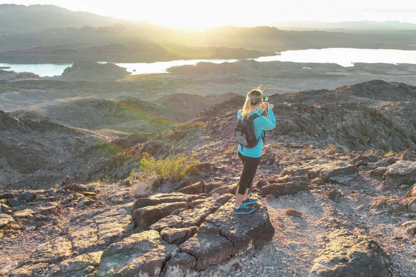Aerial view as she relaxes on mountain ridge, as the sun rises over arid desert landscape surrounding