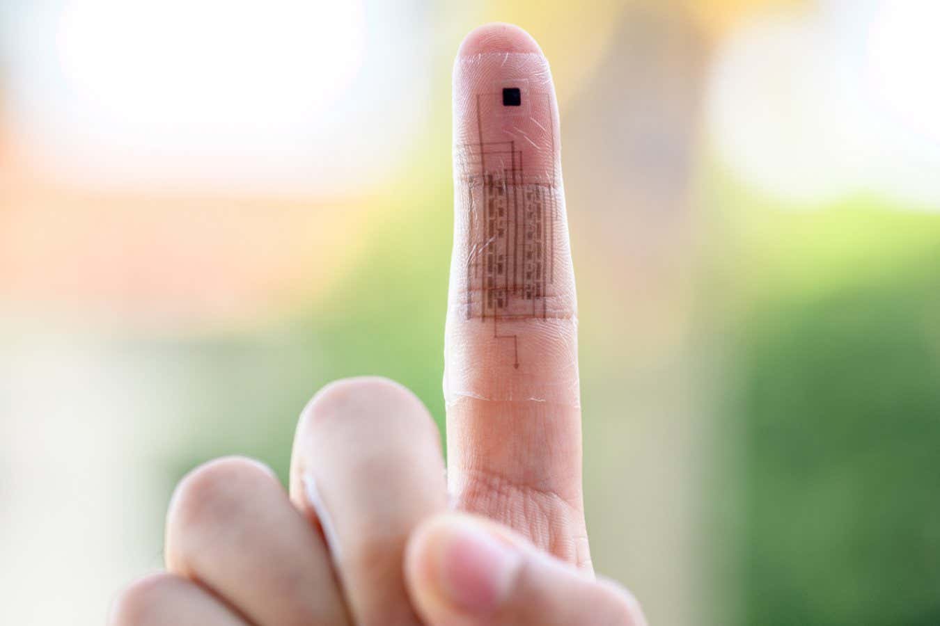 An outstretched pointer finger has a translucent skin wrapped around it. This electronic skin shows black sensors and circuitry embedded within.