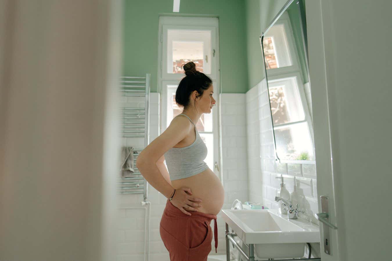 Photo of a young pregnant woman getting ready in the bathroom for the upcoming day; the daily routine of an expectant mother.